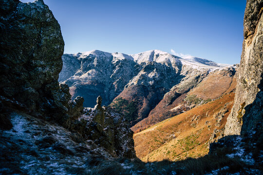 View of Golyam Kademliya Shelter surrounded by rugged rocky formations, snow-capped mountain peaks, and autumn-colored slopes under a clear blue sky in Stara Zagora, Bulgaria.