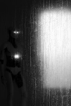 3D android emerging from shadow behind wet glass with luminous eyes and copy space