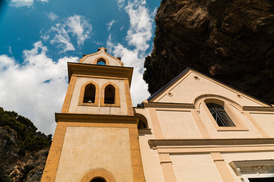 View of the Collegiate Santa Maria Maddalena church with its distinctive bell tower and facade set against a rocky cliff in Atrani, Campania, Italy.