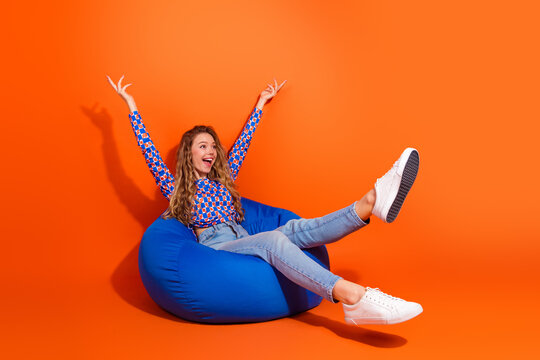 Joyful woman enjoying leisure time on a colorful beanbag against a bright orange background, celebrating happiness