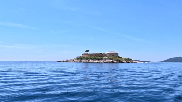 Small Island with Historic Building Surrounded by Blue Sea. Small rocky island with a historic building surrounded by calm blue sea under a clear summer sky, scenic coastal travel landscape.