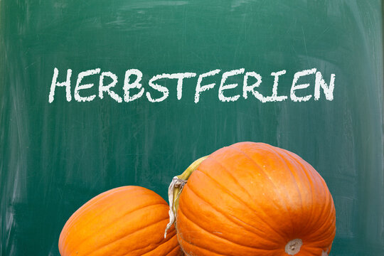 Auf einer Schultafel steht HERBSTFERIEN, am unteren Ende der Tafel befinden sich zwei K&uuml;rbisse