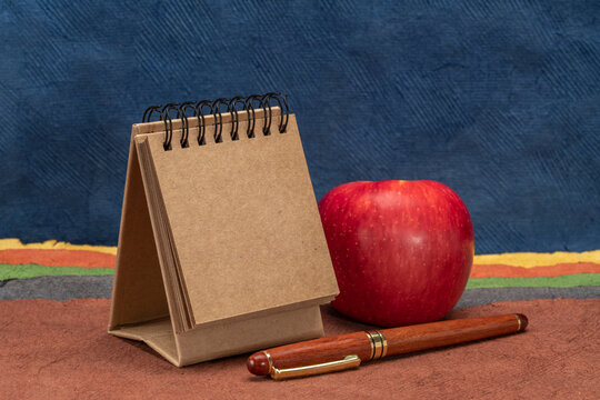small, blank desktop spiral calendar with red apple and wooden pen