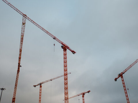 Tower cranes against gray sky at construction site, real estate development and urban growth