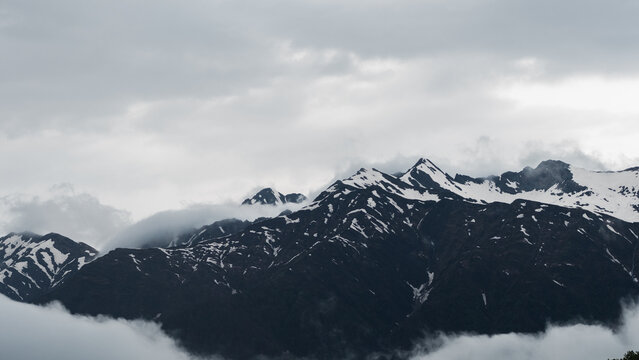 Muted mountain ridge with snow streaks above clouds, minimalist monochrome landscape