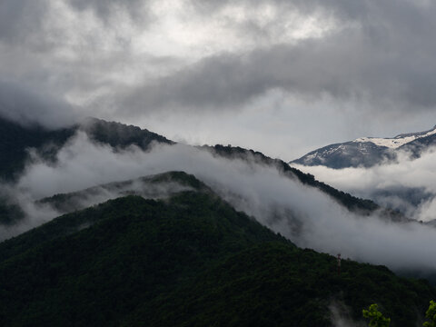 Dark mountain silhouettes wrapped in drifting fog under stormy sky, mysterious scene