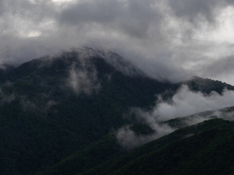 Dark wooded mountain shrouded in clouds and mist, ancient mystical fantasy landscape