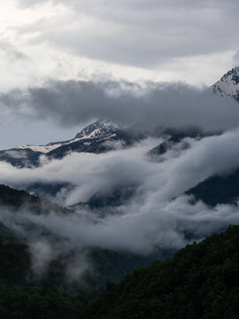 River of clouds flowing through mountain valley between snowy peaks, vertical poster
