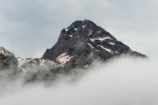 Pyramid-shaped rocky peak rising above thick fog, resilience and rising above problems