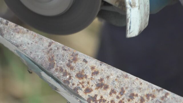 Bright sparks fly as a worker grinds a rusted steel edge at a construction site. Close-up tracking shot.