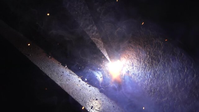 Molten metal fusing iron beams together as bright electric sparks explode during a manual construction workshop. Extreme close up macro shot.