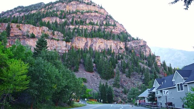 Massive tiered rock cliffs tower over highway cabins and pine trees along the north entrance to Ouray Colorado