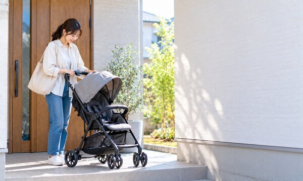 自宅の玄関でベビーカーを準備しながら子どもとの外出支度をする日本人女性