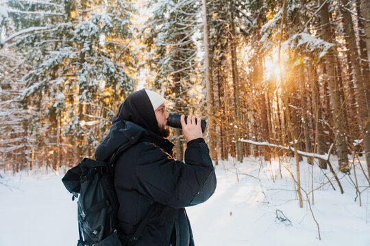 Man Drinks From a Thermos in Snowy Forest at Sunset
