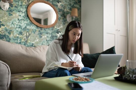 Asian freelancer making notes during video call in home office