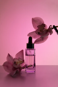 Skincare Serum Bottle With Orchid Flowers On Gradient Pink Background