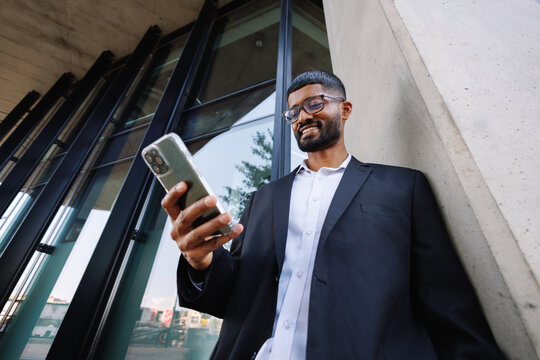 Young businessman checking smartphone, smiling in city