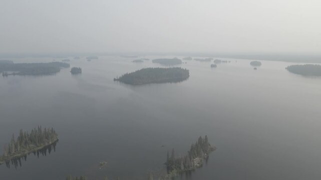 Drone flying over a large calm lake with many small islands all covered in fog or smoke
