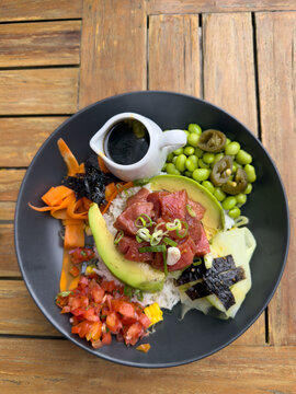 Close-up overhead view of a Tuna poke bowl with rice, avocado, edamame beans, seaweed and vegetables on a wooden table