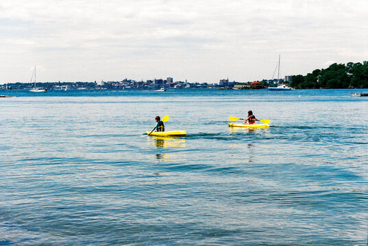Two kids kayaking with the city of Portland, Maine in the background
