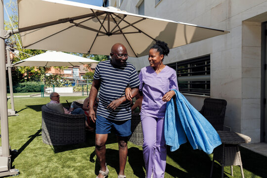 Caregiver assisting senior man walking outdoors in nursing home