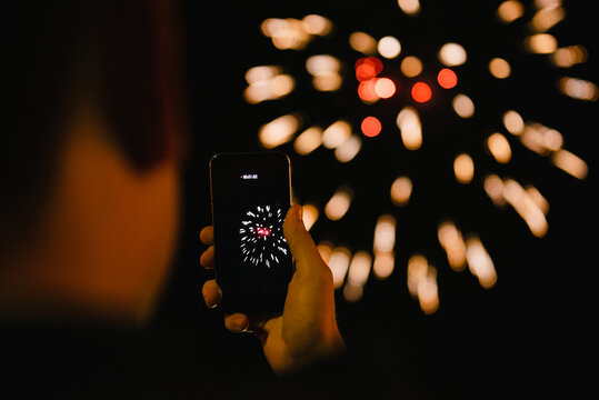 Over the shoulder view of a man filming a firework display at night on his mobile phone