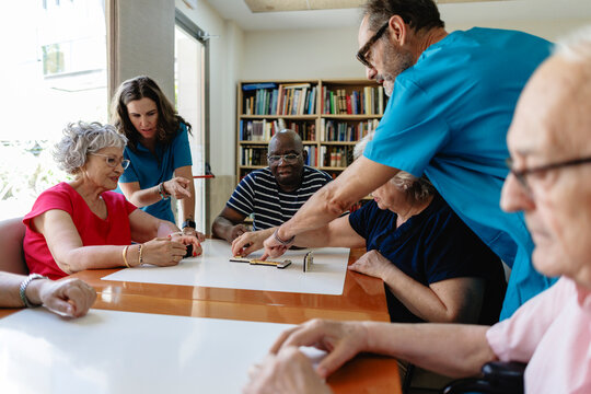 Caregivers assisting senior residents playing dominoes game