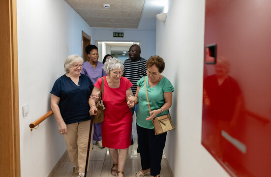 Group of senior women walking with diverse caregivers in hallway