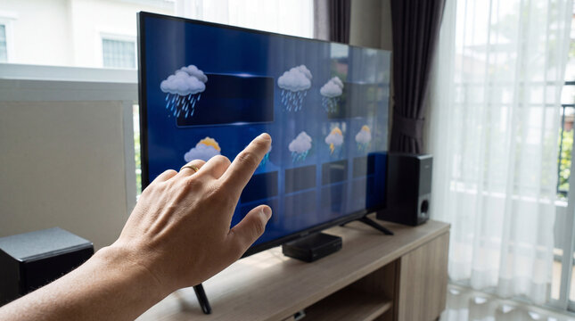 Hand pointing at weather forecast on television screen with rain clouds and icons conveying concern and urgency