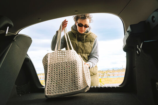 From inside to outside shot of woman putting her bag in the trunk.