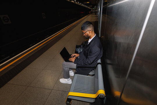 Young man working on laptop at subway platform
