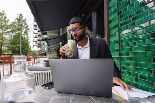 Young businessman working remotely at outdoor cafe drinking matcha
