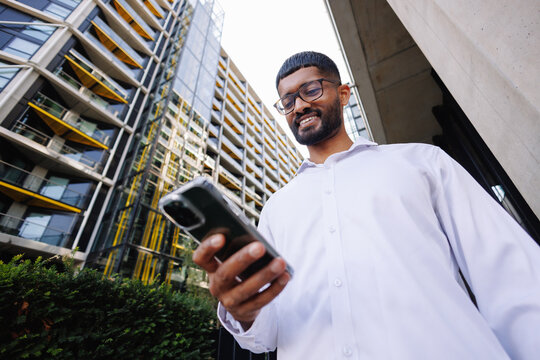Young businessman smiling, using smartphone in city