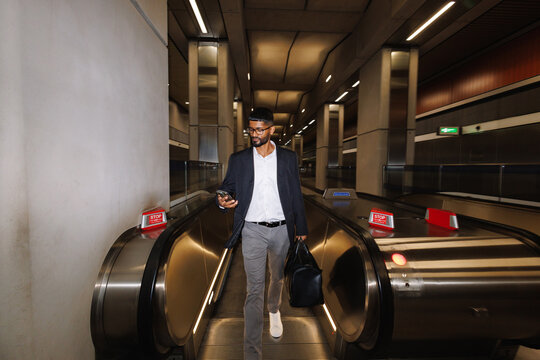 Young businessman checking smartphone walking on escalator