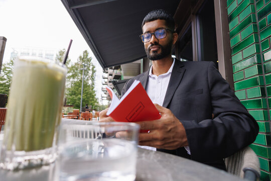 Young businessman reading book at outdoor cafe