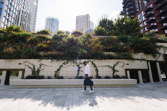 Young businessman walking with phone in green urban environment