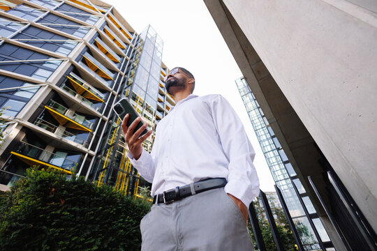 Young businessman holding smartphone looking at city buildings