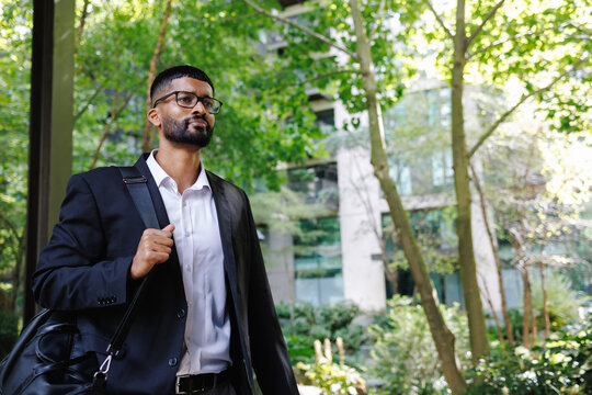 Young businessman walking in city park with bag