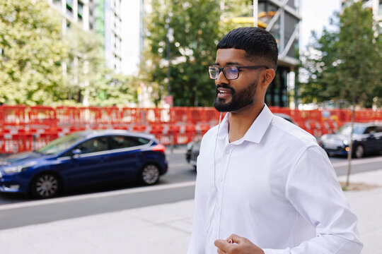 Young businessman listening to earphones walking city street