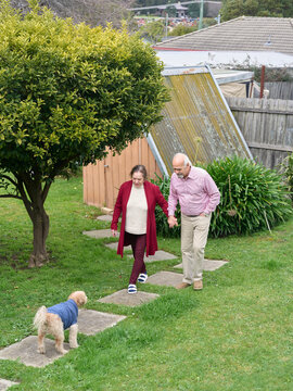 Elderly Couple Walks With a Dog in Their Backyard During the Day