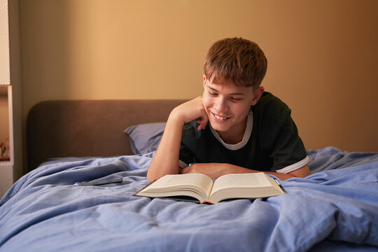 Teen Boy Lying on Bed Reading Book