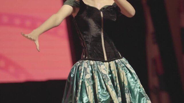 an Unrecognizable Young Asian Female Singer Performer Moving Gracefully on Stage During a Live Choral Festival Event. Wearing a Black Vintage-Style Corset Bodice and a Shiny Teal Floral Skirt