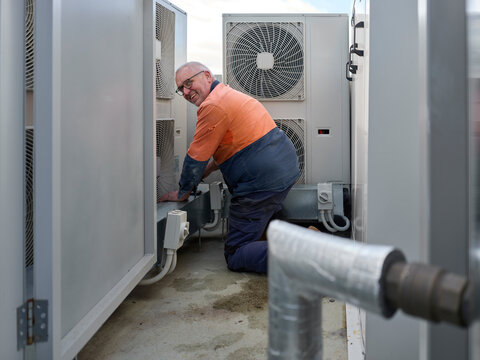 Worker Repairs HVAC Unit on Rooftop