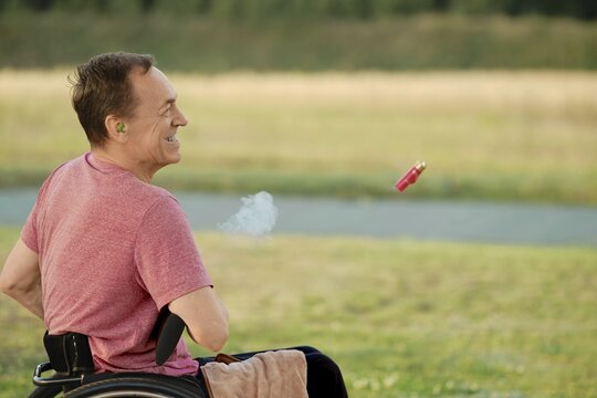 A senior man in a wheelchair opens his hunting rifle to reload the ammunition, with shell casings flying out of the barrel in the frame