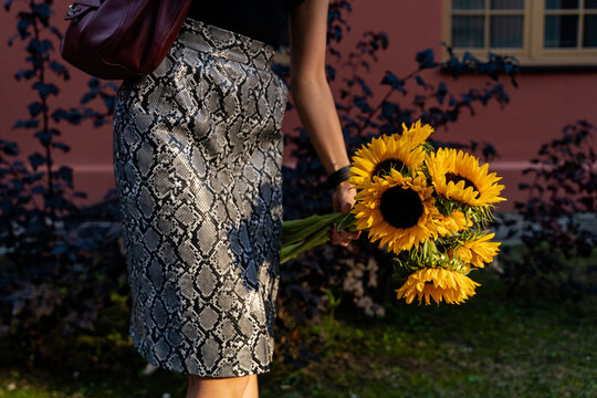 Close-up of stylish woman walking through a garden holding a bouquet of yellow sunflowers on a late summer day