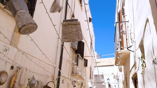 Polignano a Mare narrow charming street with hanging moka coffee makers and crochet lace decor on white houses, Puglia Italy. Handheld close up detail, authentic kitchenware. Italian Vintage Lifestyle