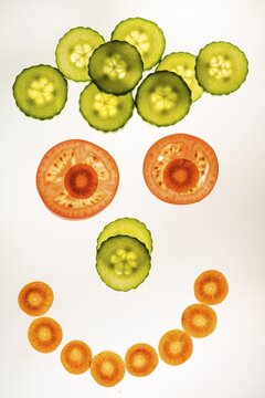 Laughing face of vegetables, smiley face, slices of cucumber, carrot and tomato, white background, food photography
