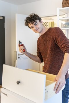 Young man doing DIY in his apartment, assembling a shelf