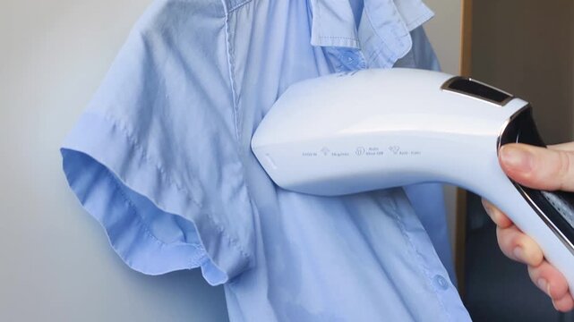 Garment care routine: ironing blue cotton shirt with handheld steam device. Fast garment steamer saves time, smooths shirt wrinkles in seconds, and provides quick, efficient clothes preparation.