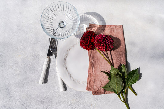 Close-up overhead view of a place setting with three dark red Pompon Dahlias on a grey concrete table